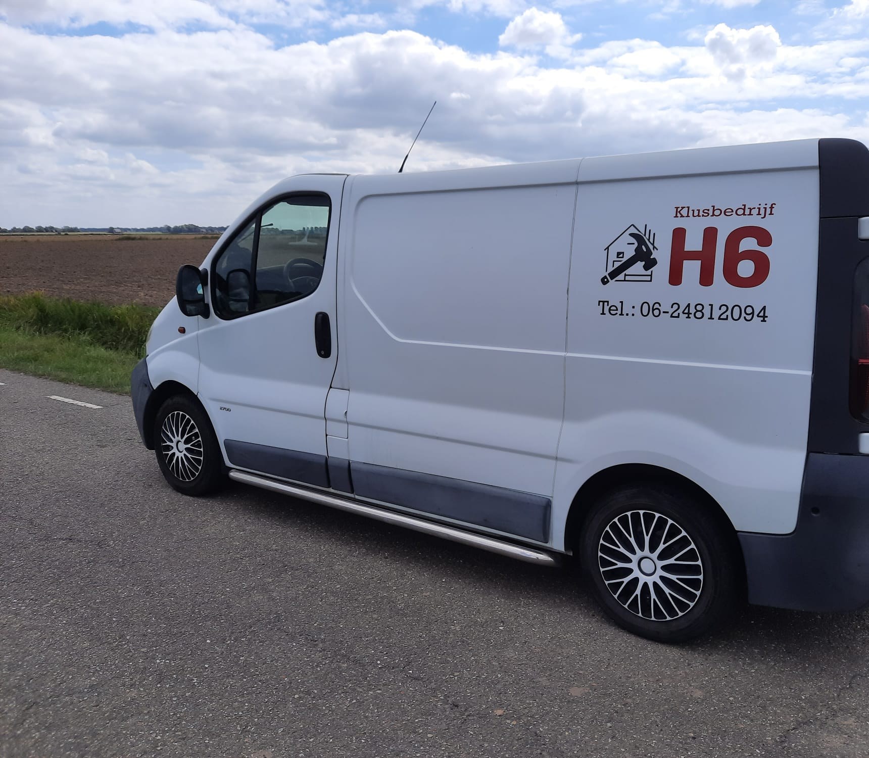 Witte bedrijfsbus van Klusbedrijf H6 met logo en telefoonnummer, langs een akker