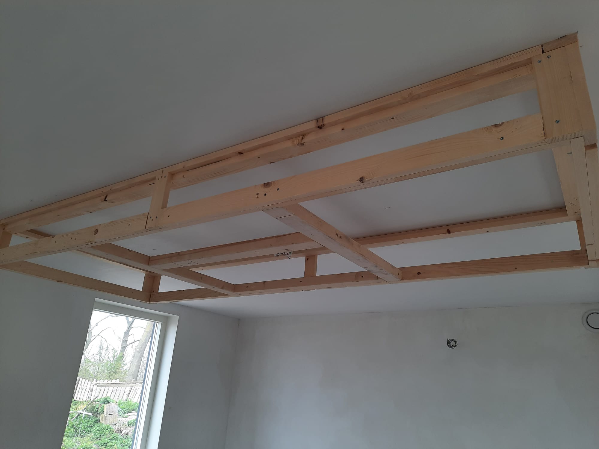 Nieuwe houten balklaag onder een wit plafond in een kamer die verbouwd wordt