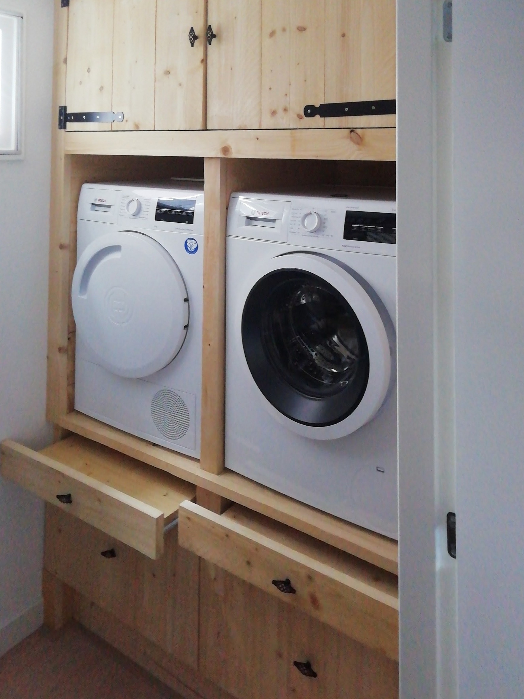 Ingebouwde houten wasmachinekast met wasmachine en droger naast elkaar, kastdeuren erboven en lades eronder